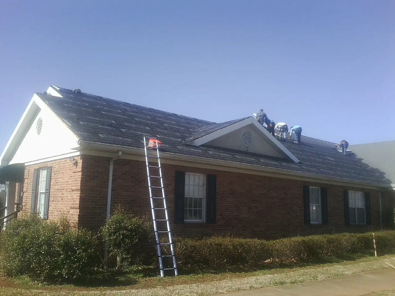 Crew tearing shingles off a brick ranch roof with a ladder set — Emergency Roof Repair work by our crew in Orange