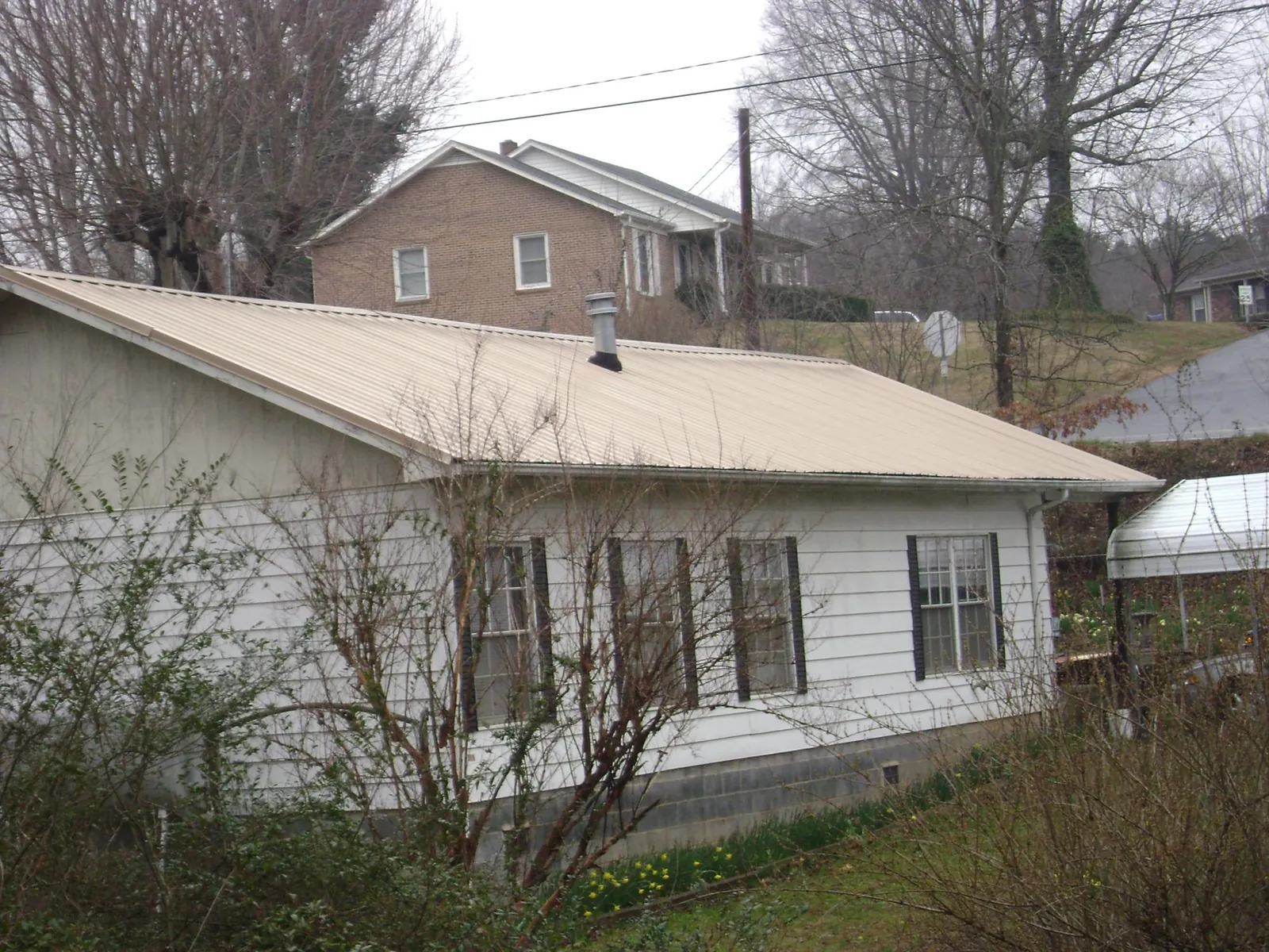 Tan metal roof on a white sided house set into a hillside — Commercial Roofing by Roofing Brothers in Orange